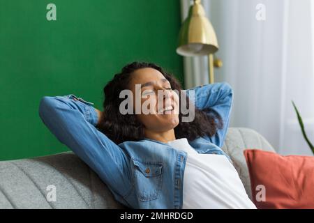 Junge hispanische Frau Hausfrau Mutter, die sich nach einem Routinetag zu Hause auf dem Sofa entspannt. Sie legte ihre Hände hinter den Kopf, schloss die Augen, entspannte sich. Stockfoto