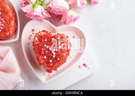 Zwei Kuchen Roter Samt in Form von Herzen auf weißem Teller, Rosenblumen und eine Tasse Kaffee auf rosafarbenem romantischem Hintergrund. Dessert-Idee für den Valentinstag, Stockfoto