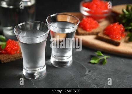 Kalter russischer Wodka und Sandwiches mit rotem Kaviar auf schwarzem Tisch, Nahaufnahme Stockfoto