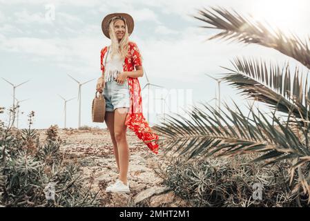 Ein blondes Mädchen, das auf einem trockenen Feld posiert, mit Windturbinen im Hintergrund. Stockfoto