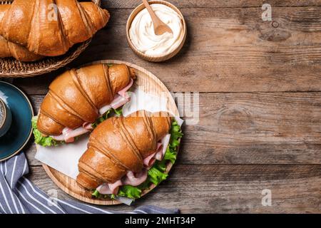 Leckere Croissant-Sandwiches mit Schinken auf einem Holztisch, flach liegend. Platz für Text Stockfoto