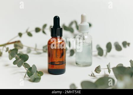 Zwei kosmetische Tropfflaschen aus Glas mit Pipette für ätherisches Öl oder Serum mit Eukalyptus auf weißem Hintergrund Stockfoto