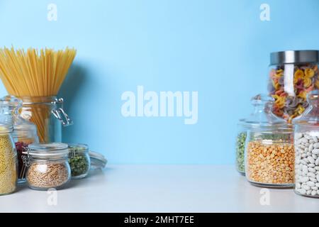 Glasgefäße mit verschiedenen Grobgrießsorten und Pasta auf einem weißen Holztisch Stockfoto