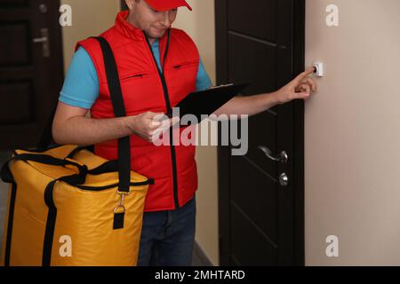 Männlicher Kurier mit Thermosack und Klemmbrett, klingelt an der Türklingel. Lebensmittellieferservice Stockfoto