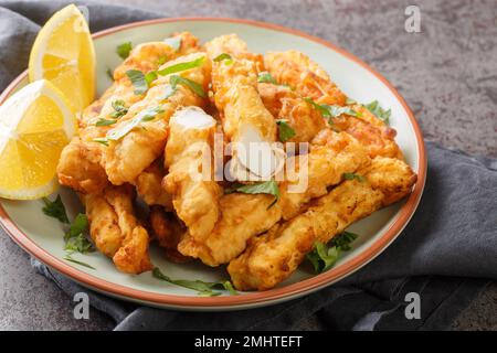 Frittierte panierte Calamari-Streifen mit Zitronennaht auf dem Teller auf dem Tisch. Horizontal Stockfoto