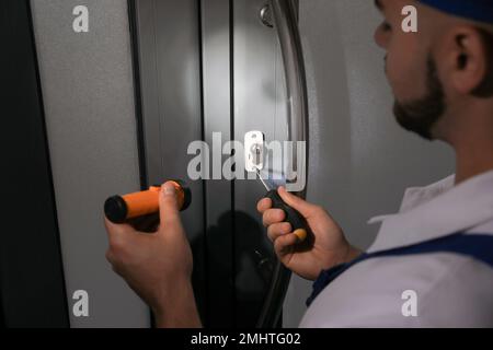 Mechaniker mit Taschenlampe, der Türschloss repariert, schließen Stockfoto