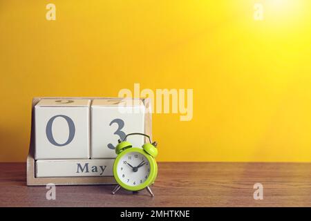 Holzkastenkalender und Wecker auf dem Tisch vor gelbem Hintergrund. Platz für Text Stockfoto