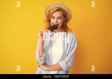 Portrait von fröhlichen lustigen Teenager-Mädchen genießt den Verzehr von kalten gefrorenen Dessert, isst köstliche Schokolade Eis, gelber Hintergrund. Stockfoto