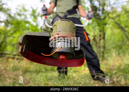 Nahaufnahme eines Mannes, der zum Rasenmähen in seinem Garten einen Rasentrimmer verwendet. Stockfoto