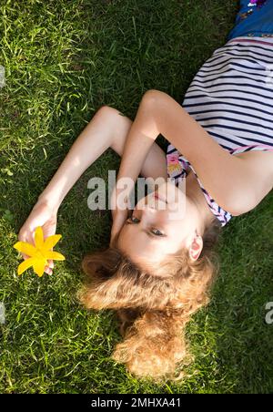 Hübsches Mädchen, 11-12 Jahre alt, liegt auf dem Rasen an einem sonnigen Sommertag, sonnt sich. Erholung mit Vergnügen in der Natur. Tag der Erde. Unachtsamkeit, Harmo Stockfoto
