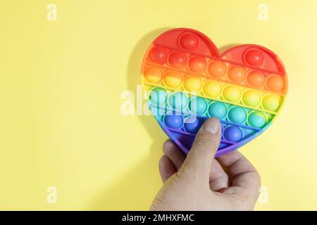 Farbenfrohes Anti-Stress-Spielzeug. Regenbogen-Sinnesfidget isoliert auf gelbem Hintergrund in der Hand während des Spiels. Spielzeug für die Entwicklung von Fine mot Stockfoto
