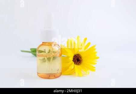 Tropfglasflaschen-Modell. Transparenter Behälter orange mit Öl für Gesicht, Lotion oder Serum, neben der Calendula Blume Cosmetology and Beauty c Stockfoto