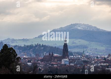 Freiburg, Deutschland. 27. Januar 2023. Der Freiburger Dom steht vor dem Hintergrund des schneebedeckten Schönbergs. Nach einer langen Zeit der Wärme über Weihnachten und Neujahr fiel in den Höhen des Schwarzwalds in den letzten Wochen Schnee. Kredit: Philipp von Ditfurth/dpa/Alamy Live News Stockfoto