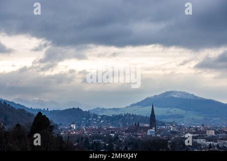 Freiburg, Deutschland. 27. Januar 2023. Der Freiburger Dom steht vor dem Hintergrund des schneebedeckten Schönbergs, mit dem Schwarzwald im Hintergrund. Nach einer langen Zeit der Wärme über Weihnachten und Neujahr fiel in den letzten Wochen in großen Höhen im Schwarzwald Schnee. Kredit: Philipp von Ditfurth/dpa/Alamy Live News Stockfoto