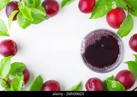 Frische Pflaumen kampotsaft in einem Glas auf Pflaumenhintergrund mit Blättern auf weißem Betonhintergrund. Herbstsommergetränke. Konserven oder Ernten. Stockfoto