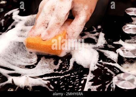 Eine Hand mit einem gelben Waschschwamm wäscht die sehr schmutzige fettige Oberfläche des Gasherds. Nach dem Schwamm bleibt eine saubere Spur zurück Stockfoto