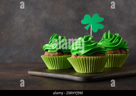 St. Patrick's Day hausgemachte Cupcakes mit grüner Schlagsahne, Shamrock und Klee auf braunem Hintergrund. Schließen. Speicherplatz kopieren. Viel Glück. Stockfoto