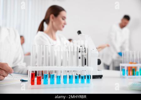 Rack mit Reagenzgläsern auf weißem Tisch und Wissenschaftlern im Labor. Medizinische Forschung Stockfoto