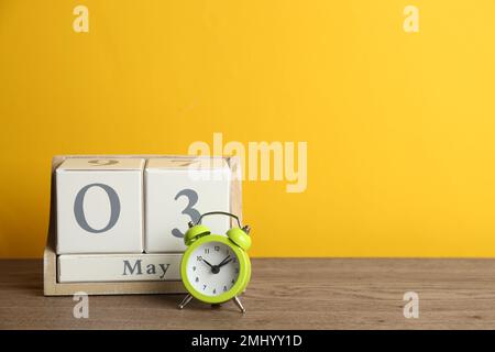 Holzkastenkalender und Wecker auf dem Tisch vor gelbem Hintergrund. Platz für Text Stockfoto