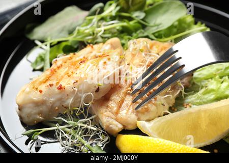 Leckerer gegrillter Fisch mit Zitrone auf dem Teller, Nahaufnahme Stockfoto