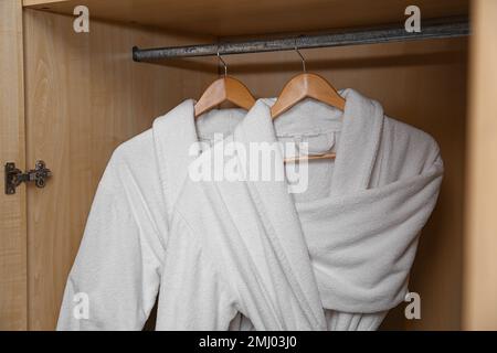 Frische weiße Bademäntel hängen in einem Holzschrank Stockfoto