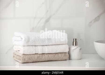 Stapel frischer Handtücher und Seifenspender auf der Arbeitsfläche im Badezimmer Stockfoto