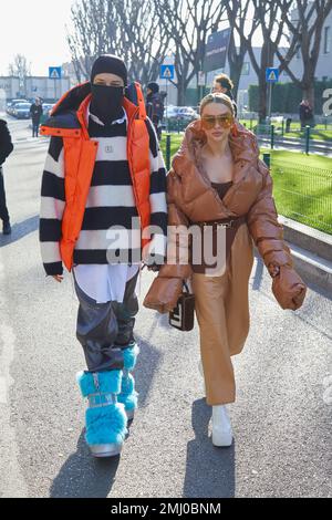 MAILAND, ITALIEN - 14. JANUAR 2023: Mann mit schwarzer Balaklava und orangefarbener Jacke und Frau mit beigefarbener gepolsterter Jacke und Hose vor Emporio Armani fash Stockfoto