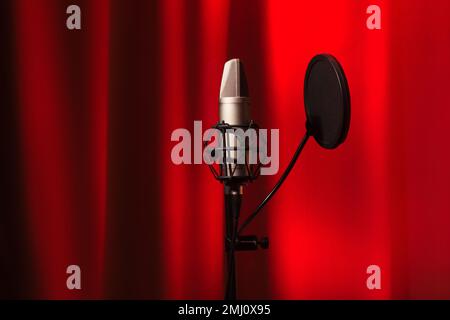 Mikrofonkondensor mit schalldichter Silhouette in Recording Studio mit rotem Neonlicht-Hintergrund, Nahaufnahme Stockfoto