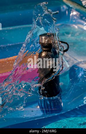 Eine schwarze Wasserflasche auf einer aufblasbaren Matratze wird von einer Welle gewaschen Stockfoto