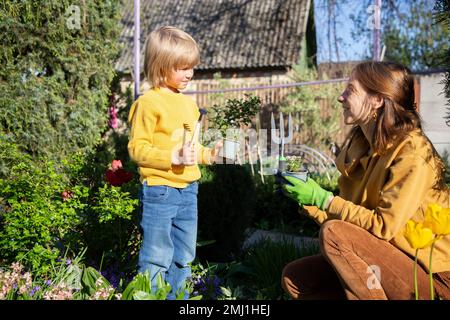 mom und kleiner Sohn arbeiten im Garten zusammen. Gelenkfamilientransplantationspflanzen im Freiland am Frühlingstag. Tag der Erde. Gärtnern mit Liebe. Nützliche Pas Stockfoto