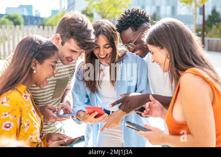 Glückliche junge Freunde, die auf dem Handy lächeln - fünf glückliche Teenager mit einem Smartphone - Lifestyle-Konzept Stockfoto