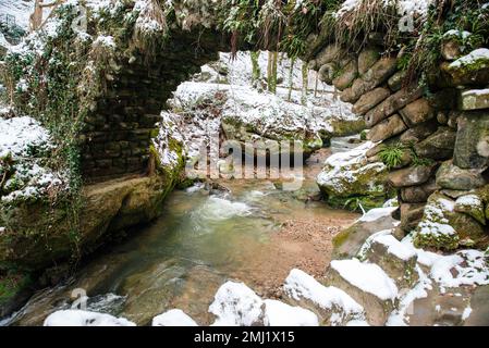 Scheissendempel-Wasserfall, Fluss Black Ernz mit schneebedeckter Steinbrücke, Müllerthal-Pfad in Waldbillig, Luxemburg im Winter Stockfoto