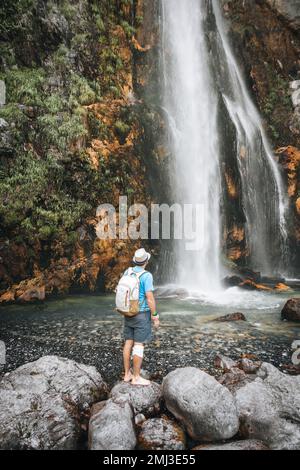 Ein Mann mit einem Rucksack steht mit einem Rucksack in der Nähe des Grunas Wasserfalls in Albanien, im Theth Nationalpark auf einer Wanderung in Albanien. Stockfoto