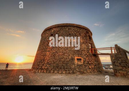 Castillo de Toston, runder Festungsturm, HDR, Hintergrundbeleuchtung, Sonnenuntergang, Eine Person von hinten am Strand mit Blick auf den Sonnenuntergang, super Weitwinkel, Westküste Stockfoto