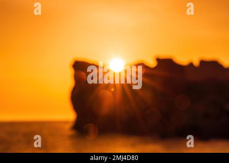 Epischer Sonnenuntergang auf dem Meer - die Sonne geht hinter dem Berg unter und alles scheint mit warmem Licht und langen Strahlen. Stockfoto