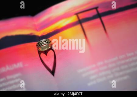 Ring in einem Buch wirft einen herzförmigen Schatten Stockfoto