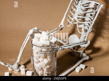 Zuckerkonsum und Einfluss des Süßsuchtbegriffs. Raffinierte Stücke weißer Süßklumpen aus Glas und totes Skelett. Weißes Todesfutter. Hohe Qualität Stockfoto