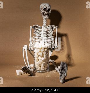 Viel Zucker essen - Konsequenzkonzept. Totes menschliches Skelett mit süßen Stücken. Hochwertiges Foto Stockfoto