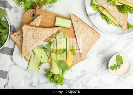 Flache Liegezusammensetzung mit leckerem Sandwich und Zutaten auf weißem Marmortisch Stockfoto