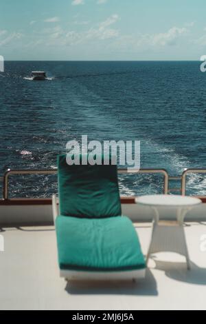 Eine vertikale Aufnahme mit selektivem Fokus auf das Boot im Hintergrund: Das Oberdeck einer Tauchyacht mit einem Sessel und einem Kaffeetisch in einem Unschärfe-Effekt Stockfoto
