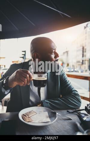 Ein vertikales Bild eines gutaussehenden schwarzen Mannes, der an einem sonnigen Morgen in einem Straßencafé Kaffee trinkt; das Porträt eines schicken afroamerikanischen Mannes, der so beschissen aussieht Stockfoto