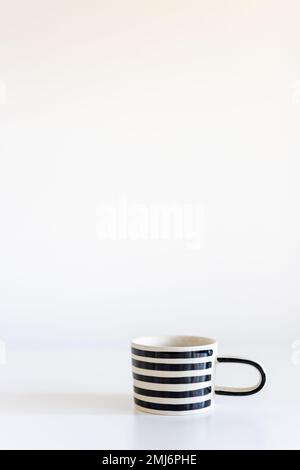 Tasse in schwarz-weißen Streifen auf einem weißen Tisch. Vertikaler Rahmen. Platz für Text. Stockfoto