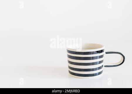 Tasse in schwarz-weißen Streifen auf einem weißen Tisch. Horizontaler Rahmen. Platz für Text. Stockfoto