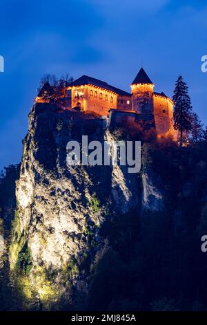 Historische mittelalterliche Burg Bled (Blejski Grad) bei Nacht mit Blick auf den touristischen Bleder See, Slowenien. Vertikale Ausrichtung Stockfoto