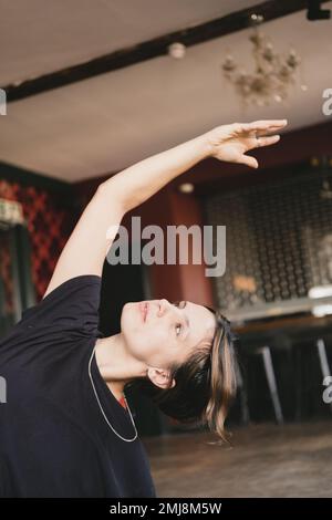 Nahaufnahme einer neuen Yoga-Lehrerin, die einen sitzenden seitlichen Körperdehnvorgang mit einem schwarzen T-Shirt im Innenbereich durchführt Stockfoto