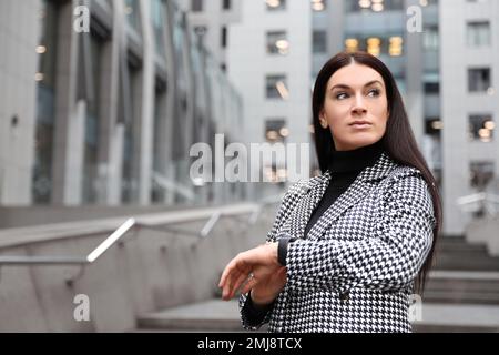 Schöne Frau in stilvollem Anzug, die Zeit im Freien prüft. Platz für Text Stockfoto
