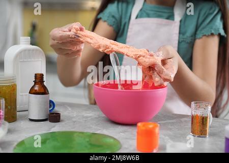 Kleines Mädchen, das Heimwerker-Schleim-Spielzeug drinnen am Tisch knete, Nahaufnahme Stockfoto