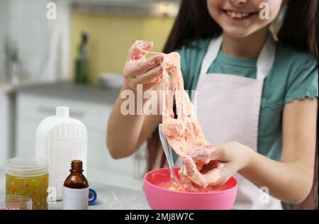 Kleines Mädchen, das Heimwerker-Schleim-Spielzeug am Tisch in der Küche knete, Nahaufnahme Stockfoto