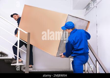 Professionelle Arbeiter, die Kühlschränke auf Treppen in Gebäuden tragen Stockfoto