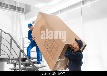 Professionelle Arbeiter, die Kühlschränke auf Treppen in Gebäuden tragen Stockfoto